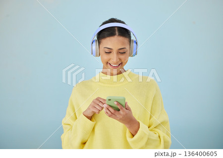 Woman with phone, headphones and mockup in studio for social media post, mobile app and streaming radio site. Smile, music media subscription and happy girl with cellphone on blue background space. Woman with phone, headphones and mockup in studio for social media post, mobile app and streaming radio site. Smile, music media subscription and happy girl with cellphone on blue background space. 136400605