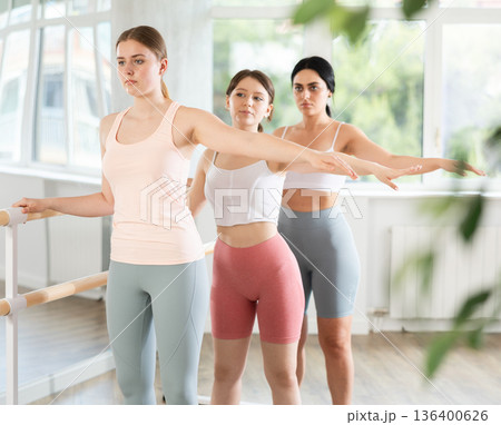 Young girl maintaining second position at ballet barre during group rehearsal 136400626