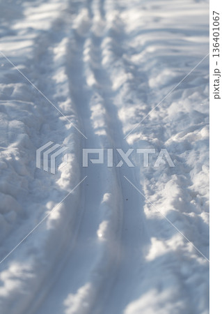 Frozen tracks cutting through snow, Car marks navigating thick snowy landscape, Wheel marks creating slender trails amid towering mounds of compacted winter snow Frozen tracks cutting through snow, Car marks navigating thick snowy landscape, Wheel marks creating slender trails amid towering mounds of compacted winter snow 136401067