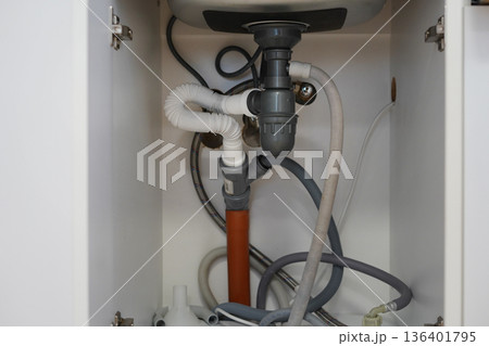 Under sink plumbing pipes and drainage system inside kitchen cabinet 136401795