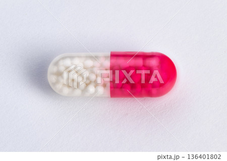 White capsule on textured background. Single pink and white capsule with glossy appearance. Studio shot showcasing capsule with textured backdrop and detailed bead visibility 136401802