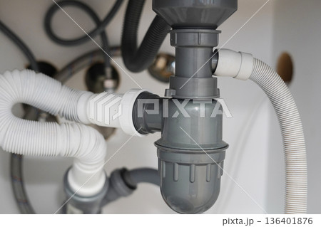 Under sink plumbing pipes and drainage system inside kitchen cabinet 136401876