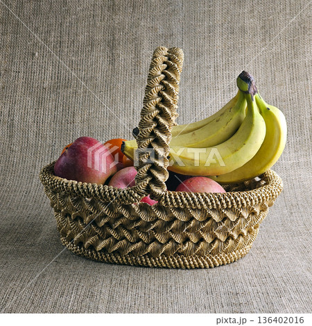 A woven straw basket against a burlap background. Close-up. Eco-friendly. Handmade basket is filled with fruit 136402016