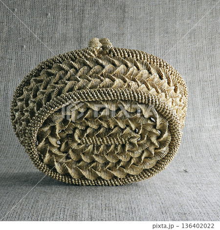 Woven straw basket against burlap background. Close-up. Eco-friendly. Handmade basket for interior decoration and use as a container for collecting fruits, vegetables, and mushrooms. Woven straw basket against burlap background. Close-up. Eco-friendly. Handmade basket for interior decoration and use as a container for collecting fruits, vegetables, and mushrooms. 136402022