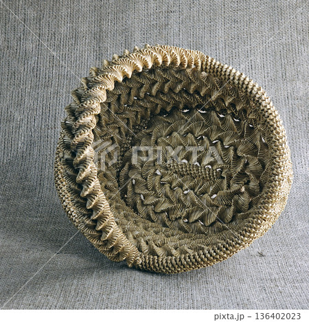 Woven straw basket against a burlap background. Close-up. Eco-friendly. Handmade basket for interior decoration and use as container for collecting fruits, vegetables, and mushrooms. 136402023