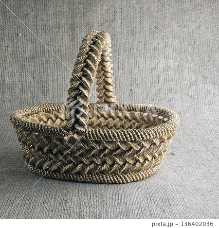 A woven straw basket against burlap background. Close-up. Eco-friendly. Handmade basket for interior decoration and use as a container for collecting fruits, vegetables, and mushrooms. 136402036