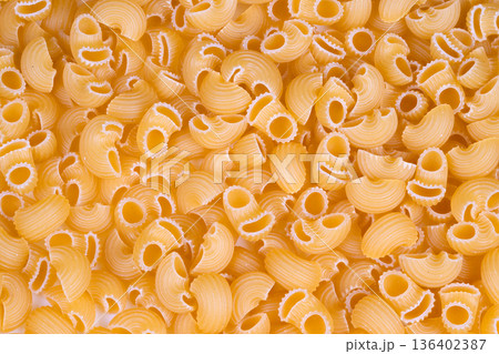 Uniform macaroni shapes showcased under specialized industrial lighting. Production line for ridged pasta with distinct surface qualities and branding applications Uniform macaroni shapes showcased under specialized industrial lighting. Production line for ridged pasta with distinct surface qualities and branding applications 136402387
