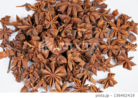 Fragmented star anise scattered on white background for food styling. Dispersed shards of star anise with seeds on white surface evoke warm beverage and baking scenes 136402419