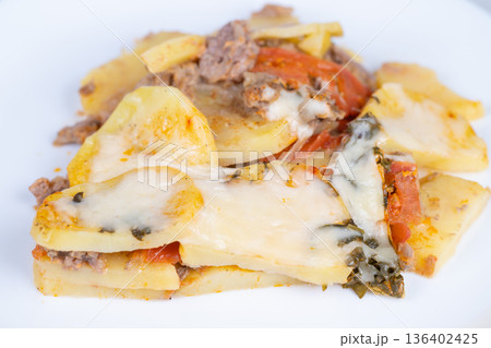 Refined layered potato dish decorated with herbs and creamy cheese topping. Sophisticated multilayered potato presentation featuring herbs and cheese in elegant style Refined layered potato dish decorated with herbs and creamy cheese topping. Sophisticated multilayered potato presentation featuring herbs and cheese in elegant style 136402425