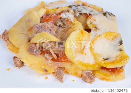 Layered potato rounds topped with sausage, melted mozzarella, warm homestyle casserole feel on plain plate, visible tomato slices and herb sprigs, comforting aroma suggested 136402473
