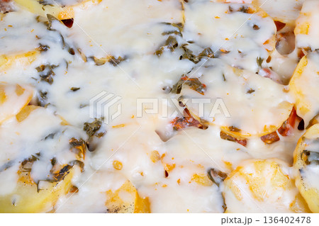 Melted cheese over potato layers. Closeup of gooey cheese on baked potatoes. Photographic capture of melted cheese cascading over golden baked potato strata for visual appeal 136402478