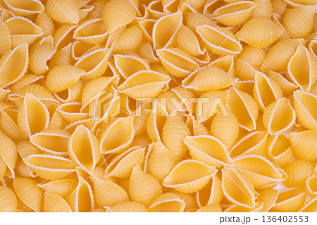 Closeup dry pasta shells texture showcasing golden ridged surfaces, semolina dust, soft shadows, warm light, kitchen pantry mood, ingredient focus, natural color palette 136402553