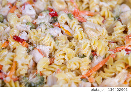 Catering rotini pasta with colorful vegetables and diced chicken, large scale presentation for events, consistent texture and appetizing sheen under bright lights 136402901
