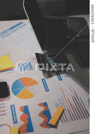 business documents on office table with tablet, smart phone and laptop and two colleagues discussing data business documents on office table with tablet, smart phone and laptop and two colleagues discussing data 136403499