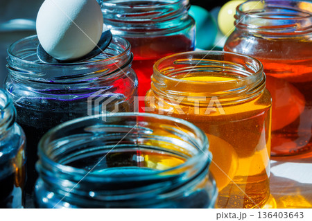 Close up of a hand using a spoon to dip a white egg into a glass jar with colorful easter dye 136403643