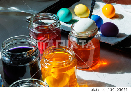 Spoon putting white egg into an orange dye jar with colorful dyed easter eggs nearby 136403651
