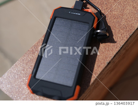 Portable solar charger resting on a surface, showcasing its robust design and eco-friendly technology for outdoor use 136403917