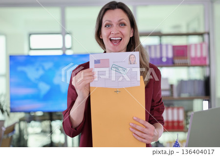 Excitement fills the air as a woman celebrates her visa approval while standing in a bright office Excitement fills the air as a woman celebrates her visa approval while standing in a bright office 136404017