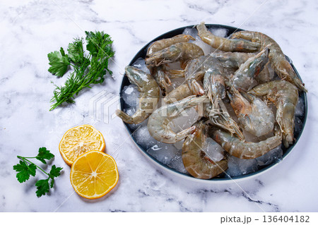 Fresh raw shrimp spread on ice with lemon and cilantro slices on a marble surface, ready to cook, no people Fresh raw shrimp spread on ice with lemon and cilantro slices on a marble surface, ready to cook, no people 136404182
