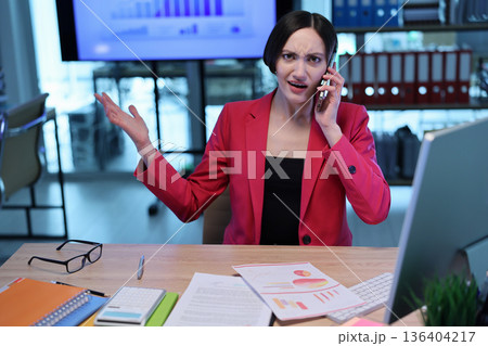 Businesswoman expressing frustration during an important phone call in a modern office setting 136404217