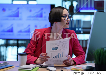 Focused analyst reviews data charts and reports in a modern office environment during a busy workday Focused analyst reviews data charts and reports in a modern office environment during a busy workday 136404229