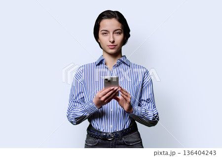 Portrait of serious teenage girl holding smartphone on white studio background Portrait of serious teenage girl holding smartphone on white studio background 136404243