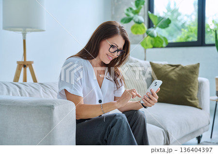 Middle aged relaxed woman on couch at home using smartphone 136404397