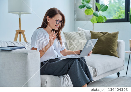 Middle aged woman working remotely, video conference, using laptop Middle aged woman working remotely, video conference, using laptop 136404398