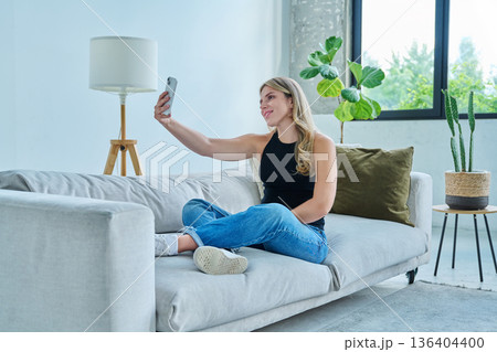 Young woman taking selfie photo using smartphone sitting on floor at home 136404400