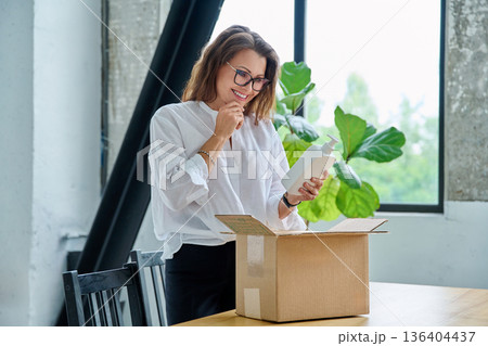 Happy satisfied woman unpacking online purchase, looking at package with cosmetics 136404437
