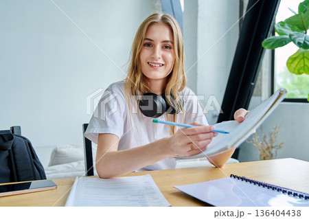 Webcam portrait female college student, sitting at home at the table with textbooks Webcam portrait female college student, sitting at home at the table with textbooks 136404438