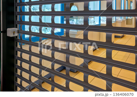 Jewelry store secured with metal roller shutter revealing illuminated luxury display cases inside 136406070