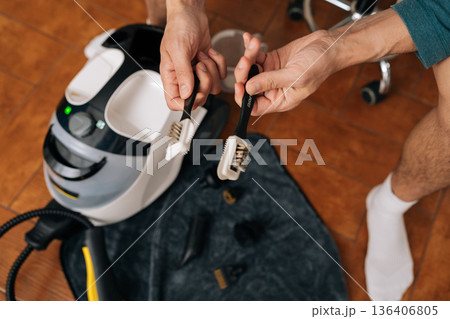 Top view of male hands holding two steam cleaner brushes, illustrating stark contrast between heavily used, dirty brush and new, clean one, emphasizing importance of maintenance in home cleaning. 136406805