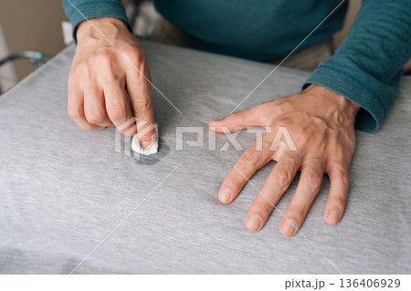 Person hands meticulously treating spill on gray fabric shirt using small white cloth soaked in cleaning agent, demonstrating household hygiene and laundry stain removal techniques. Person hands meticulously treating spill on gray fabric shirt using small white cloth soaked in cleaning agent, demonstrating household hygiene and laundry stain removal techniques. 136406929