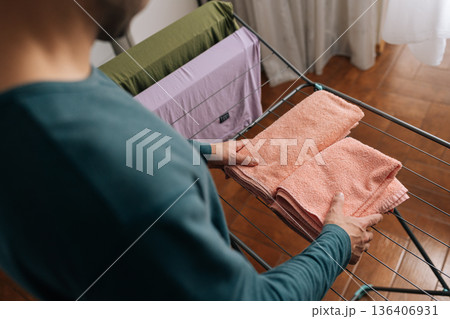 View from shoulder of unrecognizable person folding clean, soft pink towels on laundry drying rack, performing daily household chores and maintaining fresh, organized linens indoors. View from shoulder of unrecognizable person folding clean, soft pink towels on laundry drying rack, performing daily household chores and maintaining fresh, organized linens indoors. 136406931