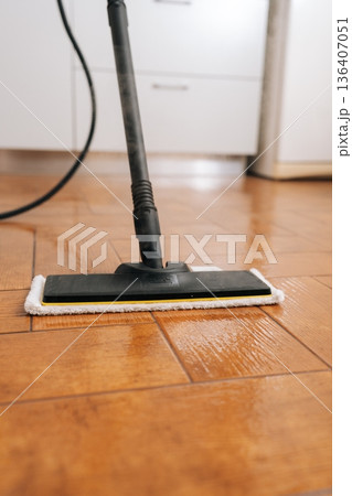 Steam mop cleaning wooden floor, emitting hot vapor for effective sanitization and deep cleaning, ensuring sparkling and hygienic home environment. Concept of household chores and housework. 136407051