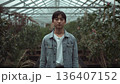 Young Person Stands Inside a Greenhouse With Plants Surrounded During Cloudy Day 136407152