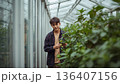 Young Person Works in a Greenhouse Surrounded by Plants During Daytime in a Garden Area 136407156