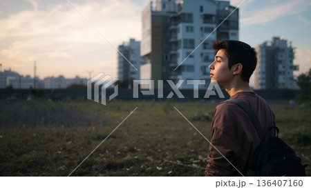 Person Standing in a Field Looking at Buildings During Sunset in an Urban Area 136407160
