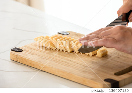 A hands slice small Parmigiano cheese pieces on a light wooden cutting board 136407180