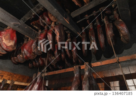 A rustic smokehouse scene showing rows of hanging cured meats 136407185