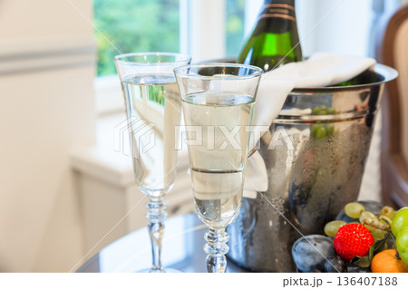 A champagne bottle resting in a frosty ice bucket beside a crystal flutes 136407188