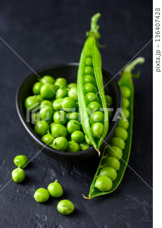 Green peas in black ceramic bowl with scattered pods Green peas in black ceramic bowl with scattered pods 136407428