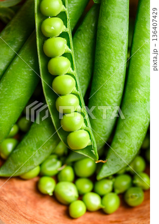 Green peas overflowing from wooden bowl with pods 136407429