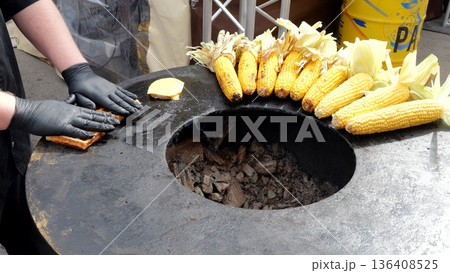 Vendor flipping waffles, Cook flips waffles by corn, Food vendor skillfully flips waffles near corn and barbecue area, Merchant wearing gloves carefully turns waffles beside corn on grill surface Vendor flipping waffles, Cook flips waffles by corn, Food vendor skillfully flips waffles near corn and barbecue area, Merchant wearing gloves carefully turns waffles beside corn on grill surface 136408525