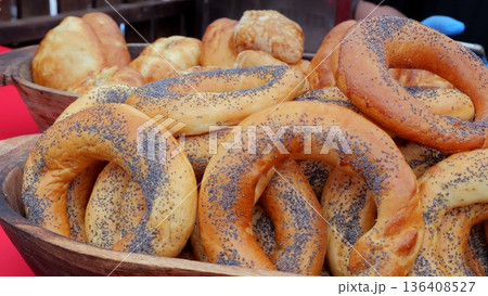 Poppy seed bagels piled in basket, golden crusts, chewy centers, wooden bowl, vendor stall backdrop, red cloth, morning light, authentic street market vibe, freshly baked aroma inviting visitors 136408527