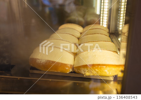 Fresh traditional Italian pastries arranged in a bakery display case, showcasing layered desserts with creamy filling under warm interior lighting. Fresh traditional Italian pastries arranged in a bakery display case, showcasing layered desserts with creamy filling under warm interior lighting. 136408543