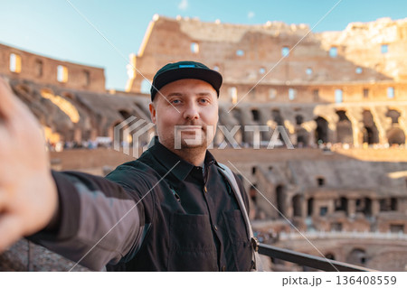 Smiling male tourist taking a selfie at the Colosseum in Rome, Italy. Famous ancient Roman amphitheater and popular historical landmark visited by tourists from around the world. 136408559