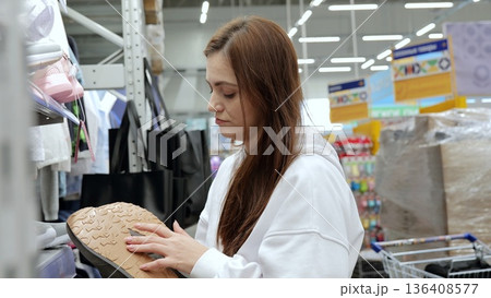 Woman meticulously inspecting the sole of a sneaker while shopping for shoes in a supermarket, making an informed decision among a range of products Woman meticulously inspecting the sole of a sneaker while shopping for shoes in a supermarket, making an informed decision among a range of products 136408577