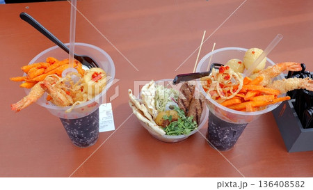 Closeup seafood cups with lemon, crispy tempura shrimp, noodle salad, sliced chili and creamy sauce, camera gear visible suggesting tasting review, warm natural light and casual outdoor festival table Closeup seafood cups with lemon, crispy tempura shrimp, noodle salad, sliced chili and creamy sauce, camera gear visible suggesting tasting review, warm natural light and casual outdoor festival table 136408582